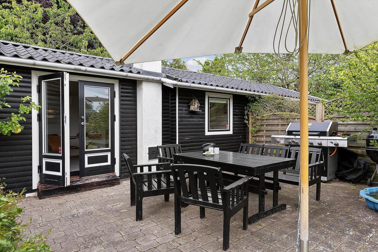 Terrace with table, chairs, and umbrella. Grill and plants are visible.