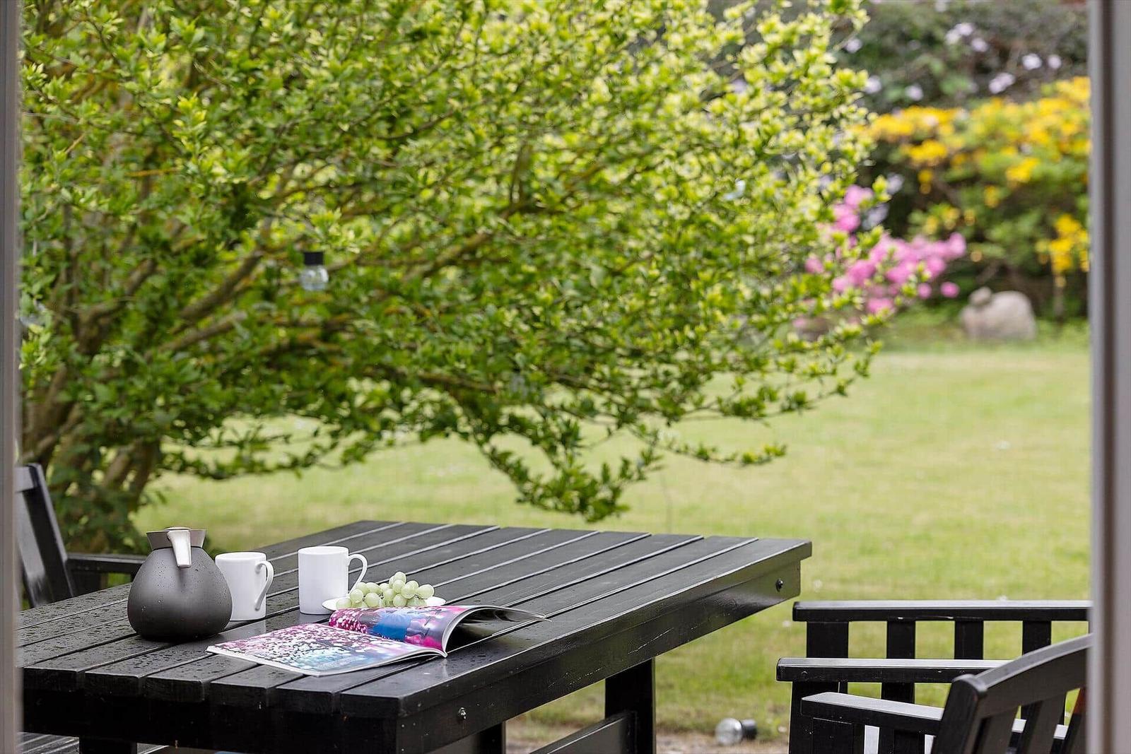 Black table with kettle, mugs, and magazine in the garden.