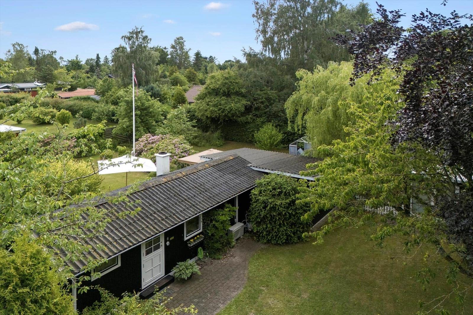Black house with gray roof, surrounded by green trees and a garden.