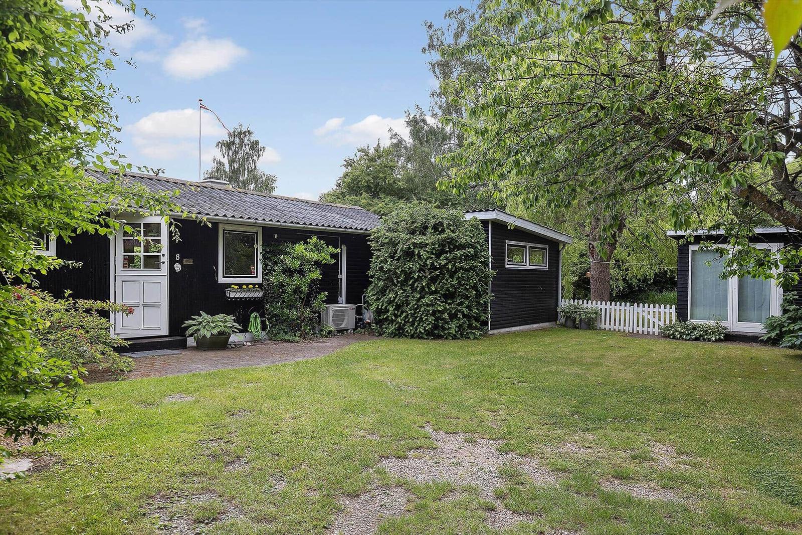 Black house with white door and green garden. Flag on pole. White fence.