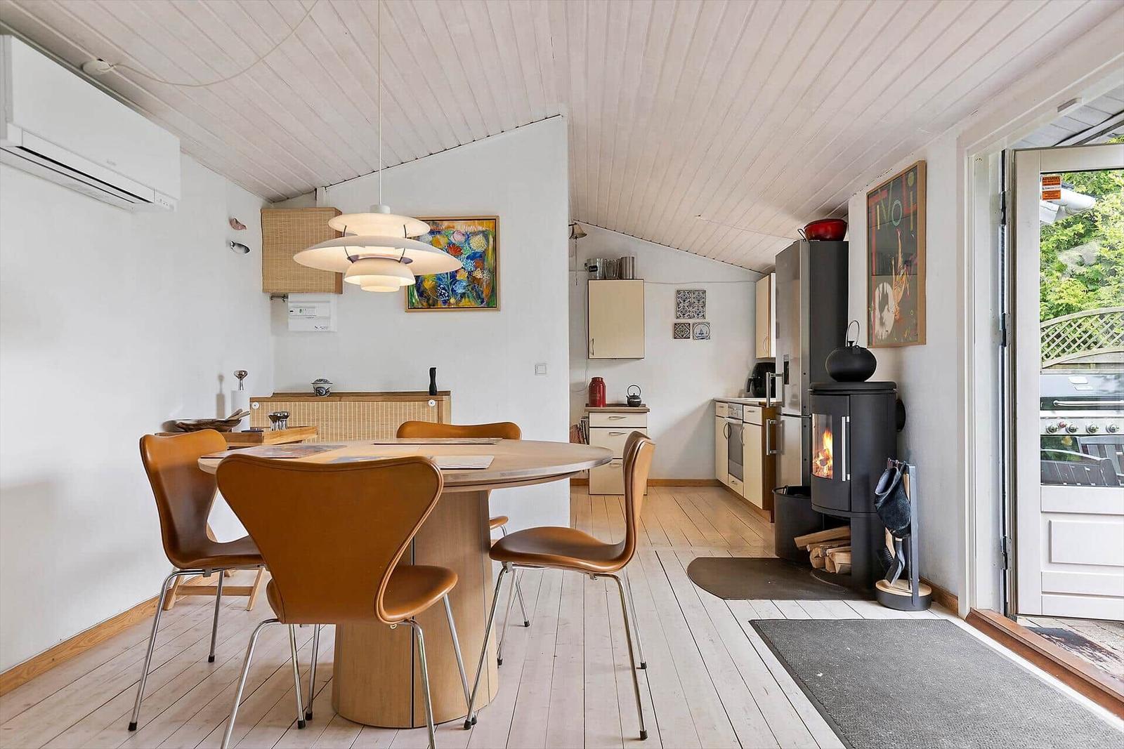 Dining area with round table and brown chairs, kitchen and wood stove in background.