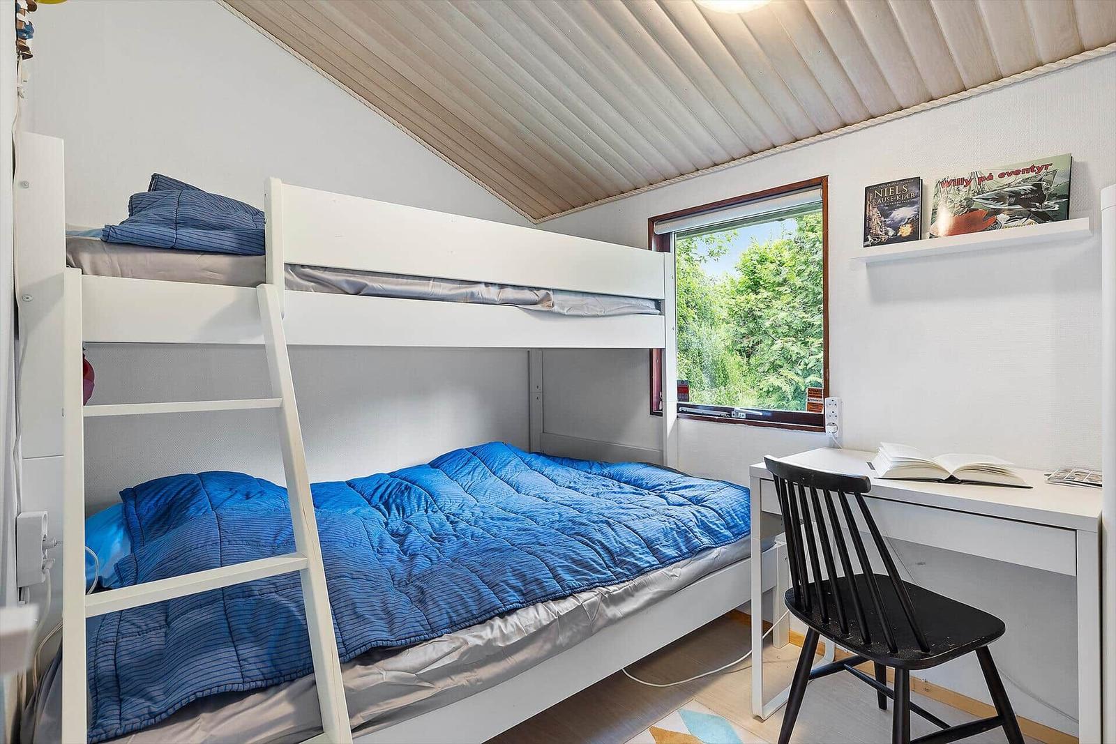 Room with bunk bed, desk, and window with view of greenery.