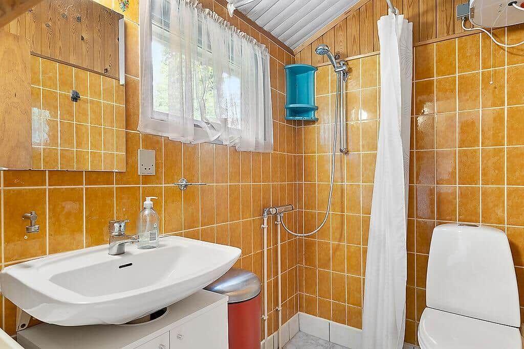 Bathroom with shower, sink and toilet. Walls are covered with orange tiles.
