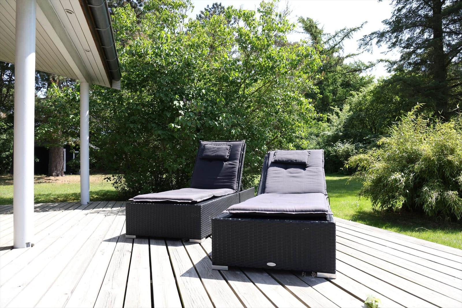 Two black sun loungers on a wooden terrace with green surroundings.