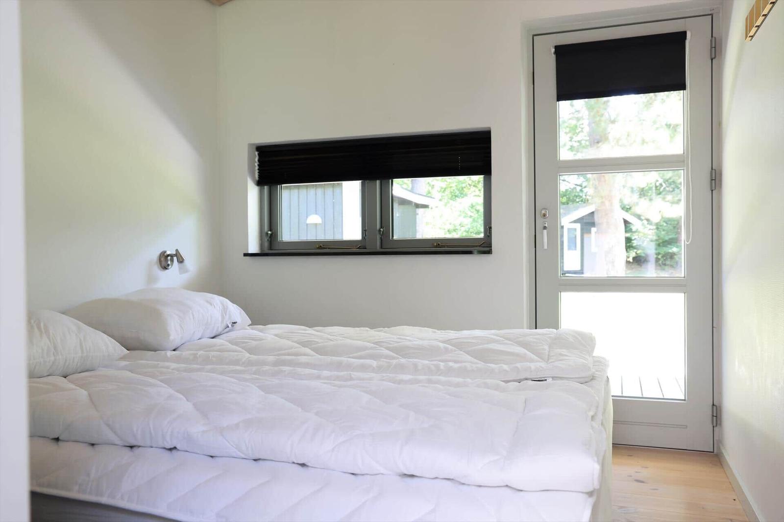 Bedroom with white bed, window, and door leading to outdoor area.