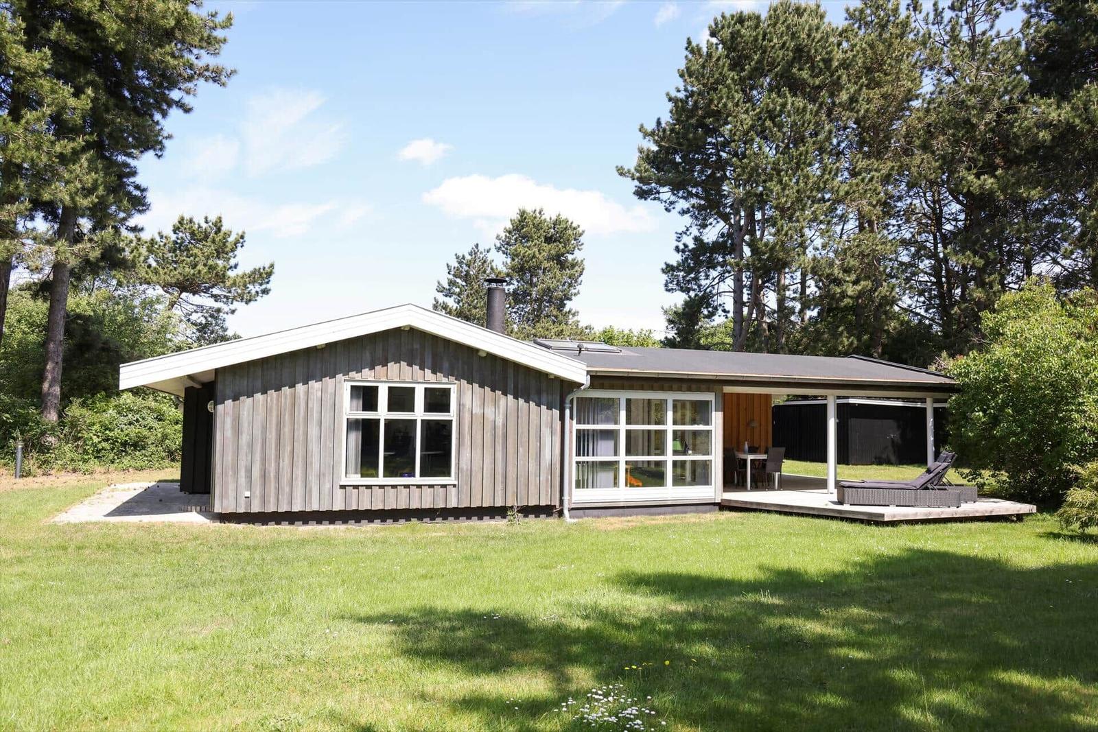 Wooden house with terrace, garden, and surrounding trees.