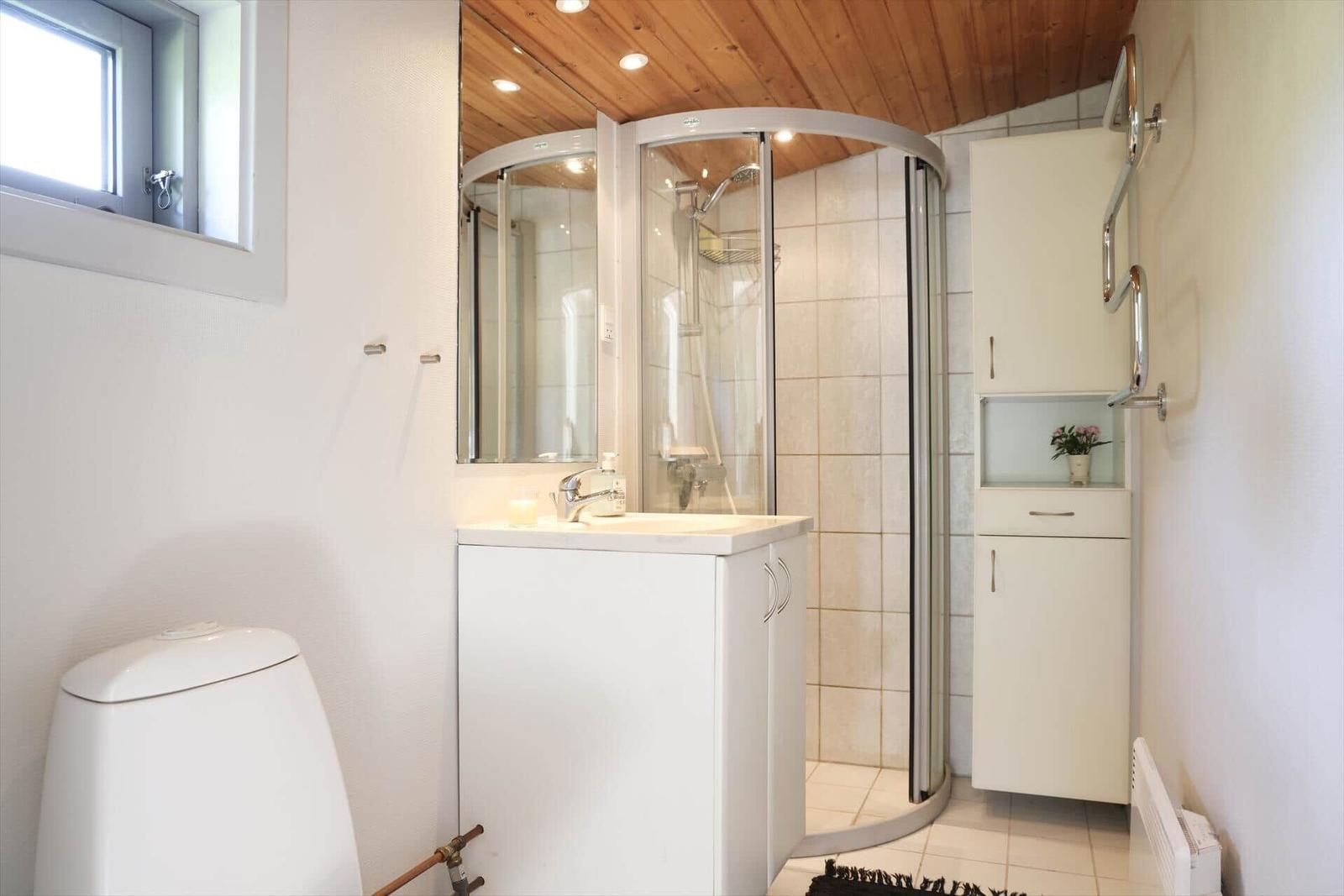 Bathroom with shower, sink and toilet. Wooden ceiling and white tiles.
