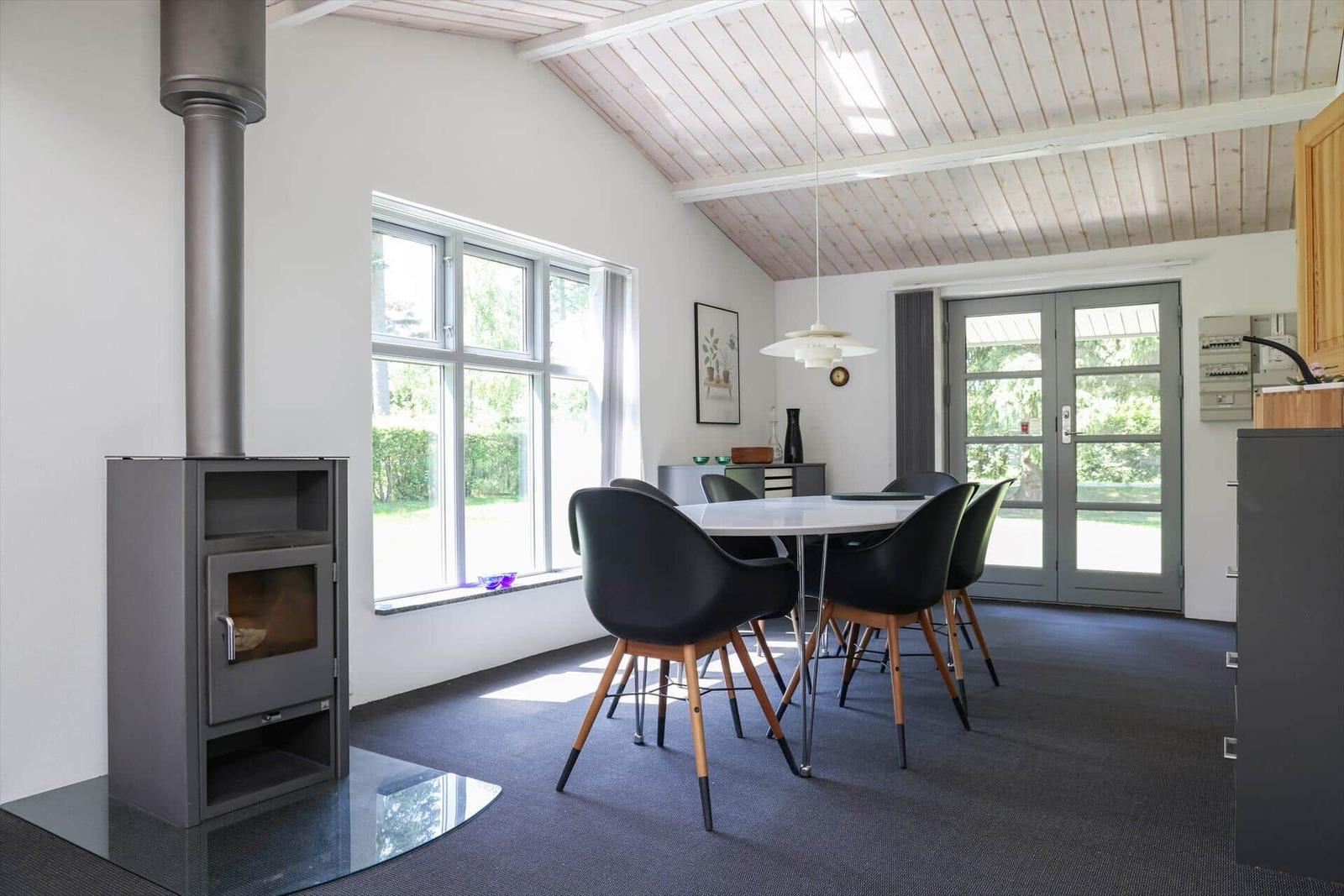 Dining room with wooden ceiling, table, chairs, and wood stove. Windows and glass doors provide ample light.
