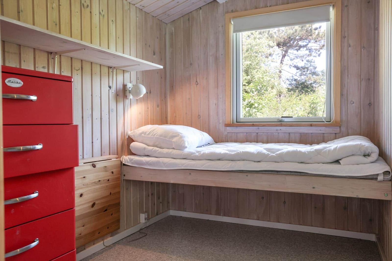 A bedroom with wooden walls, window, and red dresser.