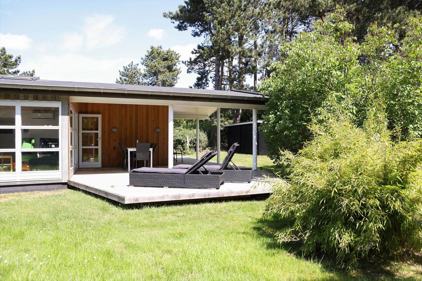 Deck with loungers and table under roof. Lawn and trees surround the house.