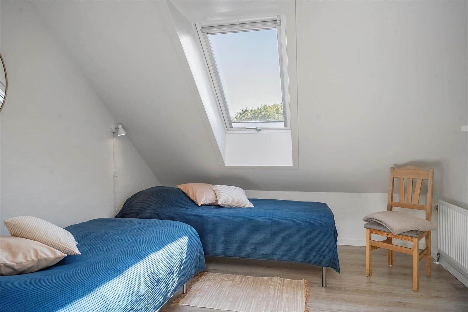 Room with two beds, skylight, and wooden chair.