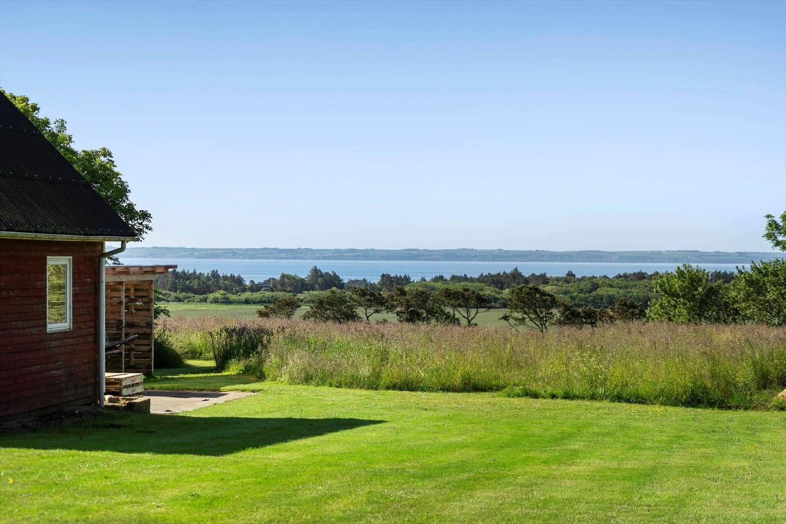 Red house with view of sea and green fields.