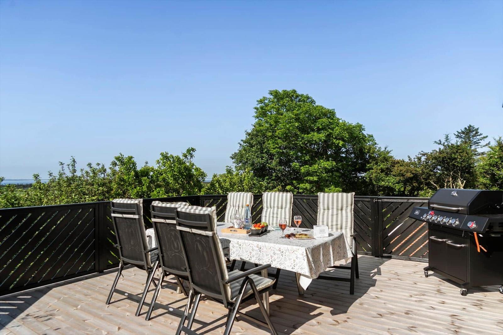 Deck with dining table, chairs, and grill. View of green trees and horizon.