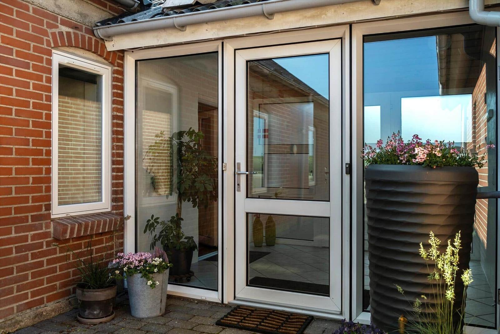 Entrance with glass doors and plants in front of a brick facade.