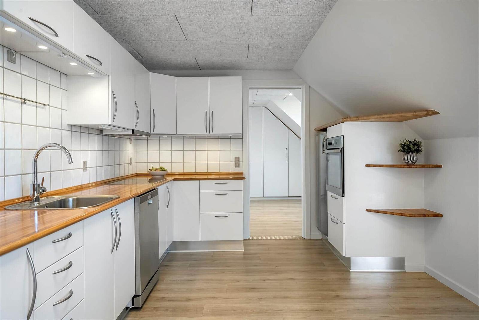 Modern kitchen with wooden surfaces and white cabinets under a sloped ceiling.