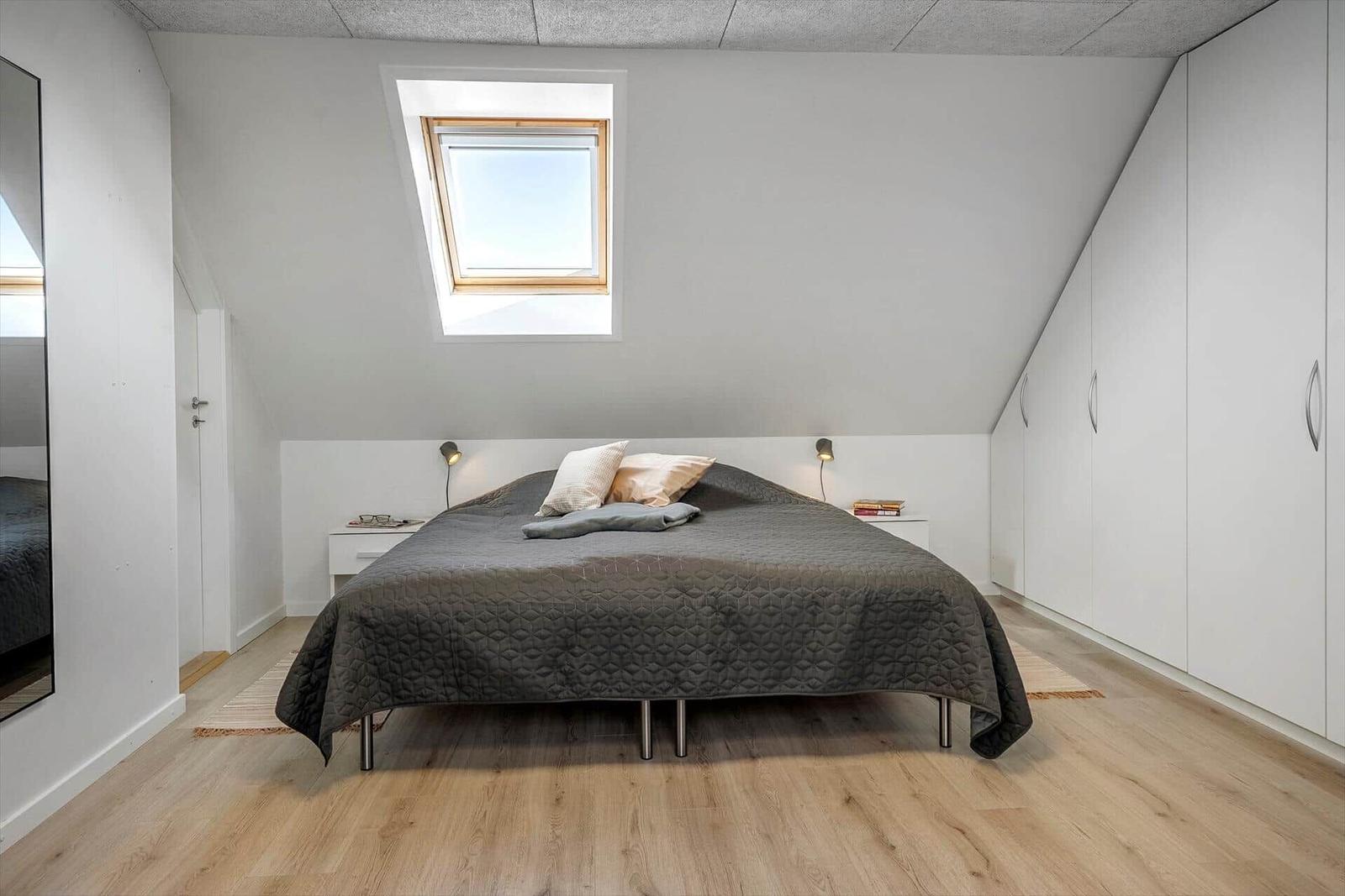 Bedroom with skylight, bed, wardrobe, and wooden floor.