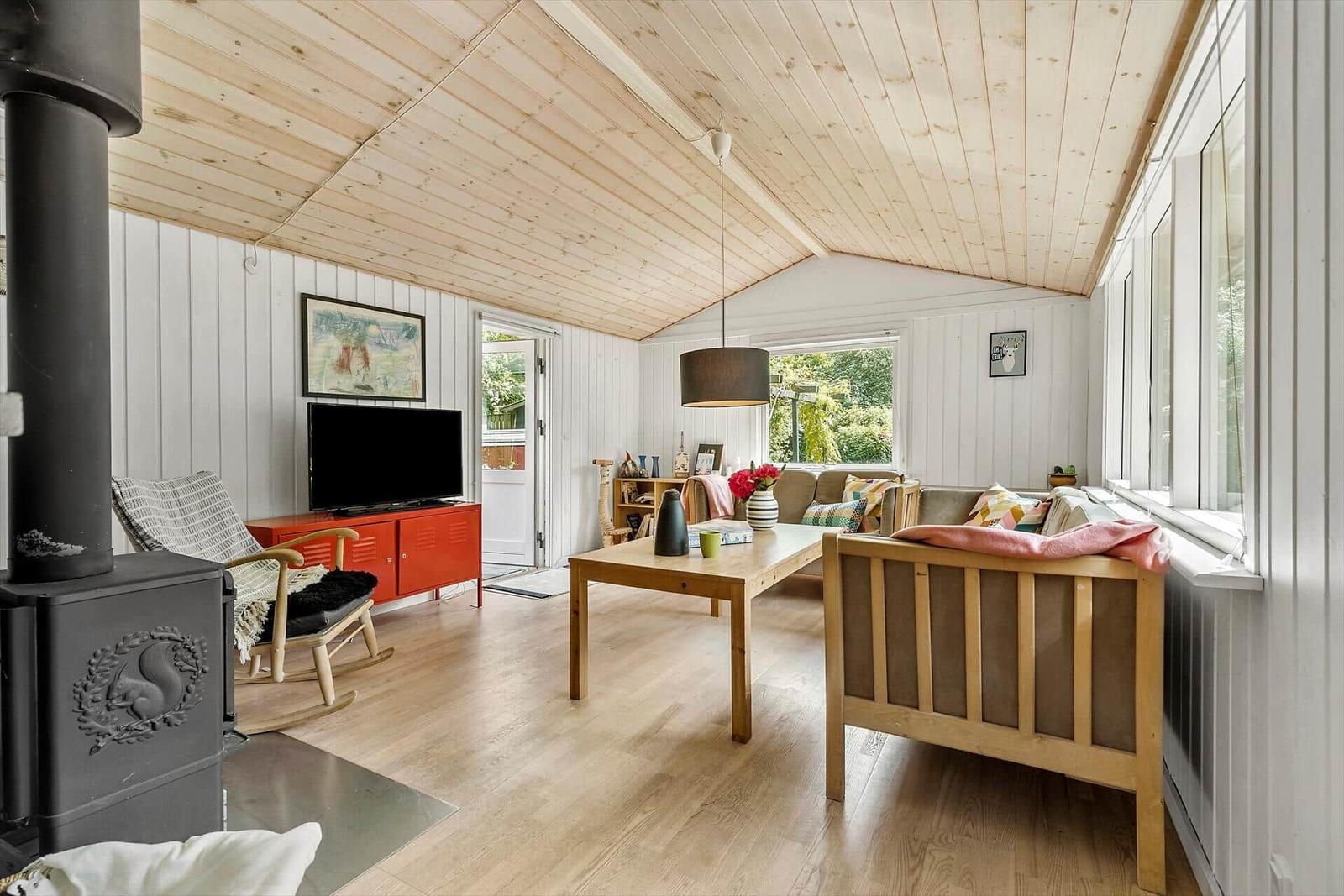 Wohnzimmer mit Holzdecke, Sofa, Tisch und Kaminofen.