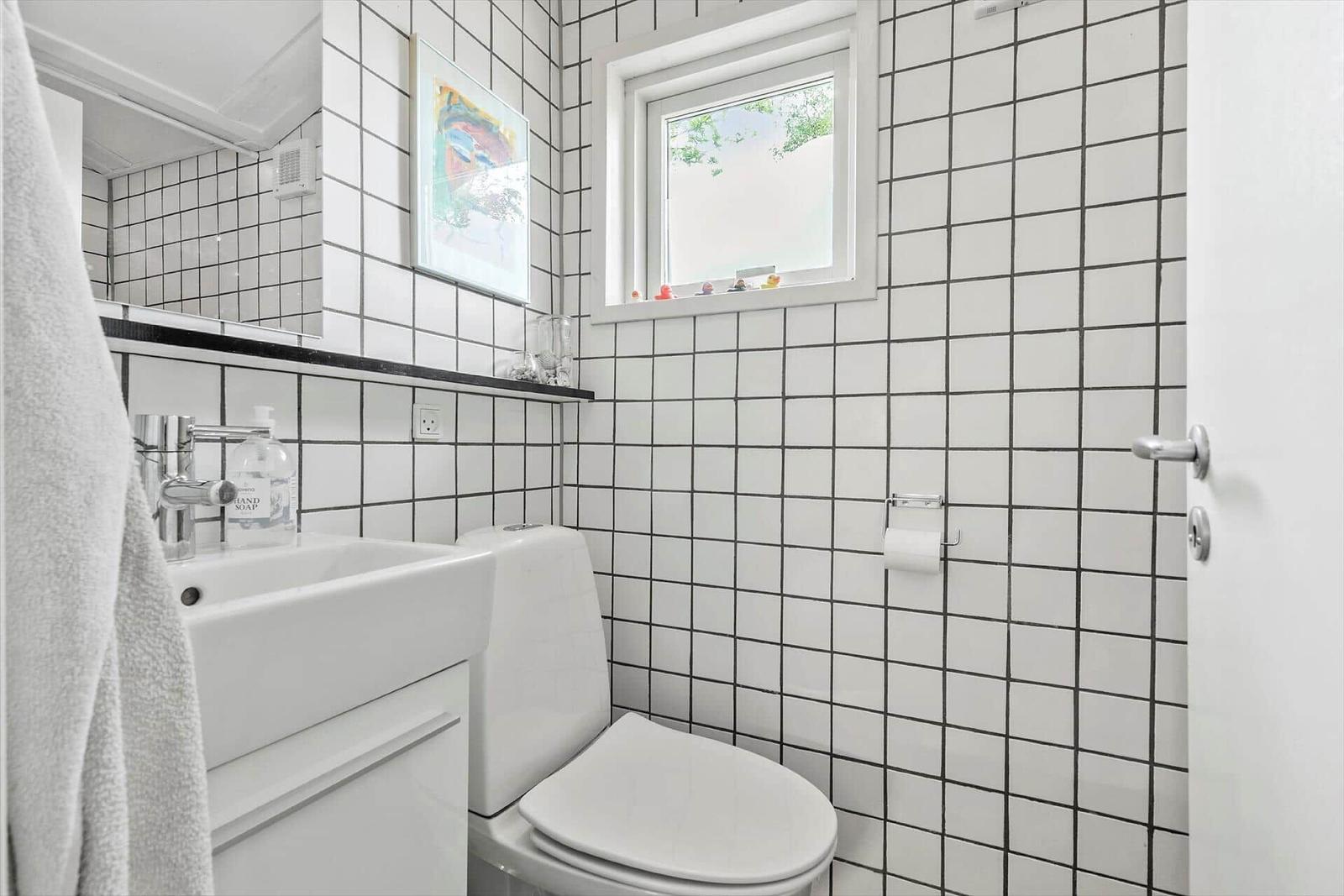 Badezimmer mit weißer Fliesenwand, Toilette, Waschbecken und Fenster.