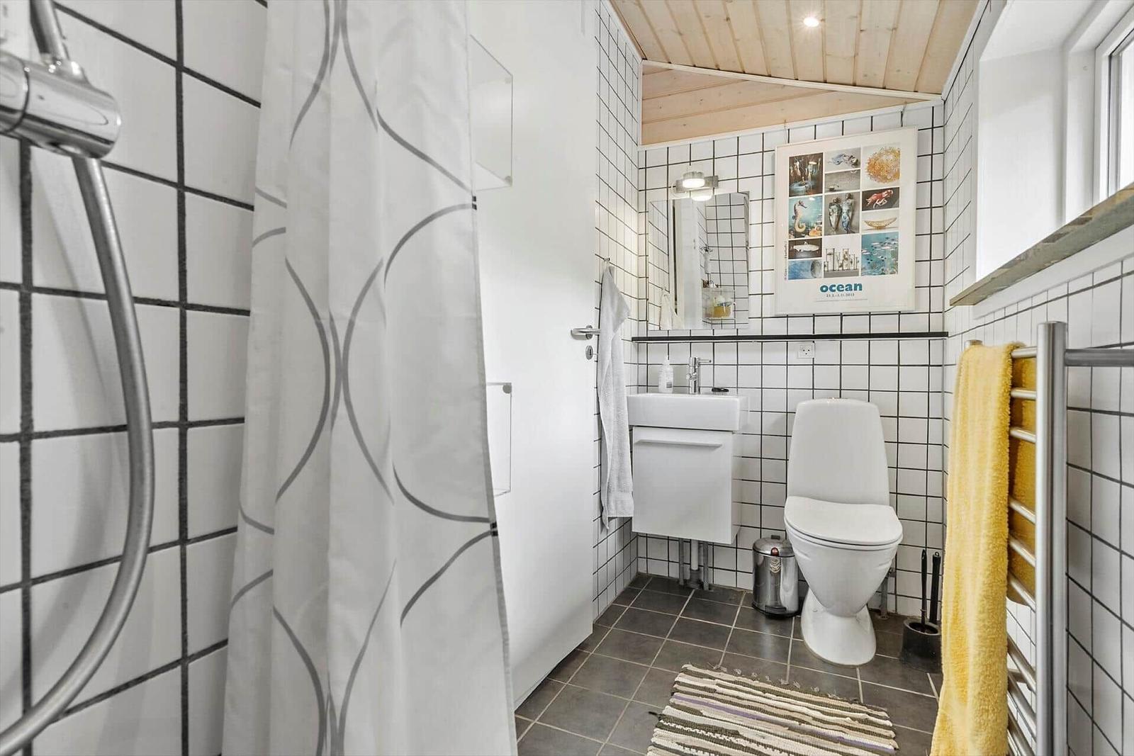 Badezimmer mit Dusche, Toilette und Waschbecken. Weiße Fliesen und Holzdecke.
