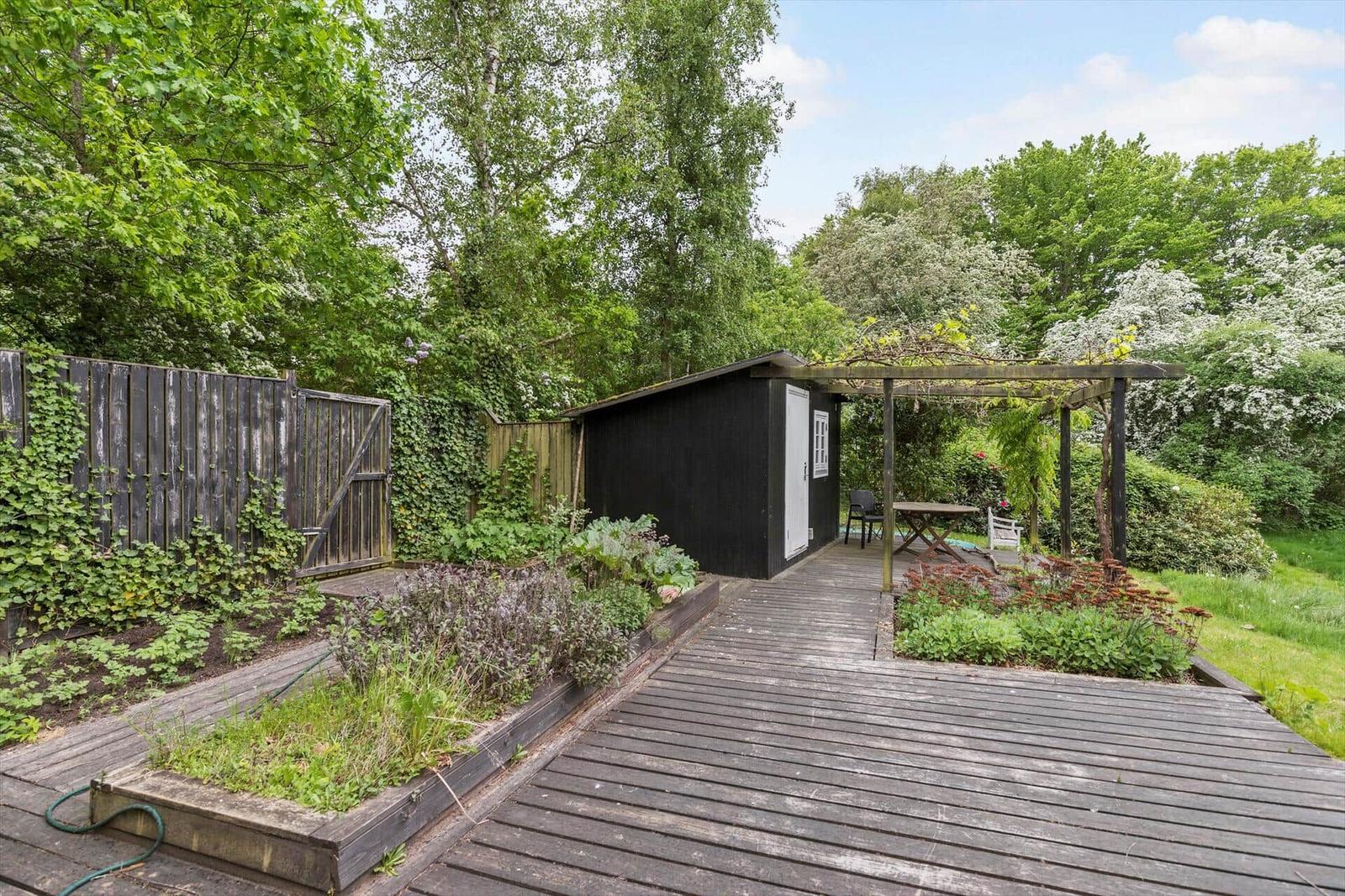 Holzterrasse mit Garten, Pergola und kleinem Haus im Grünen.