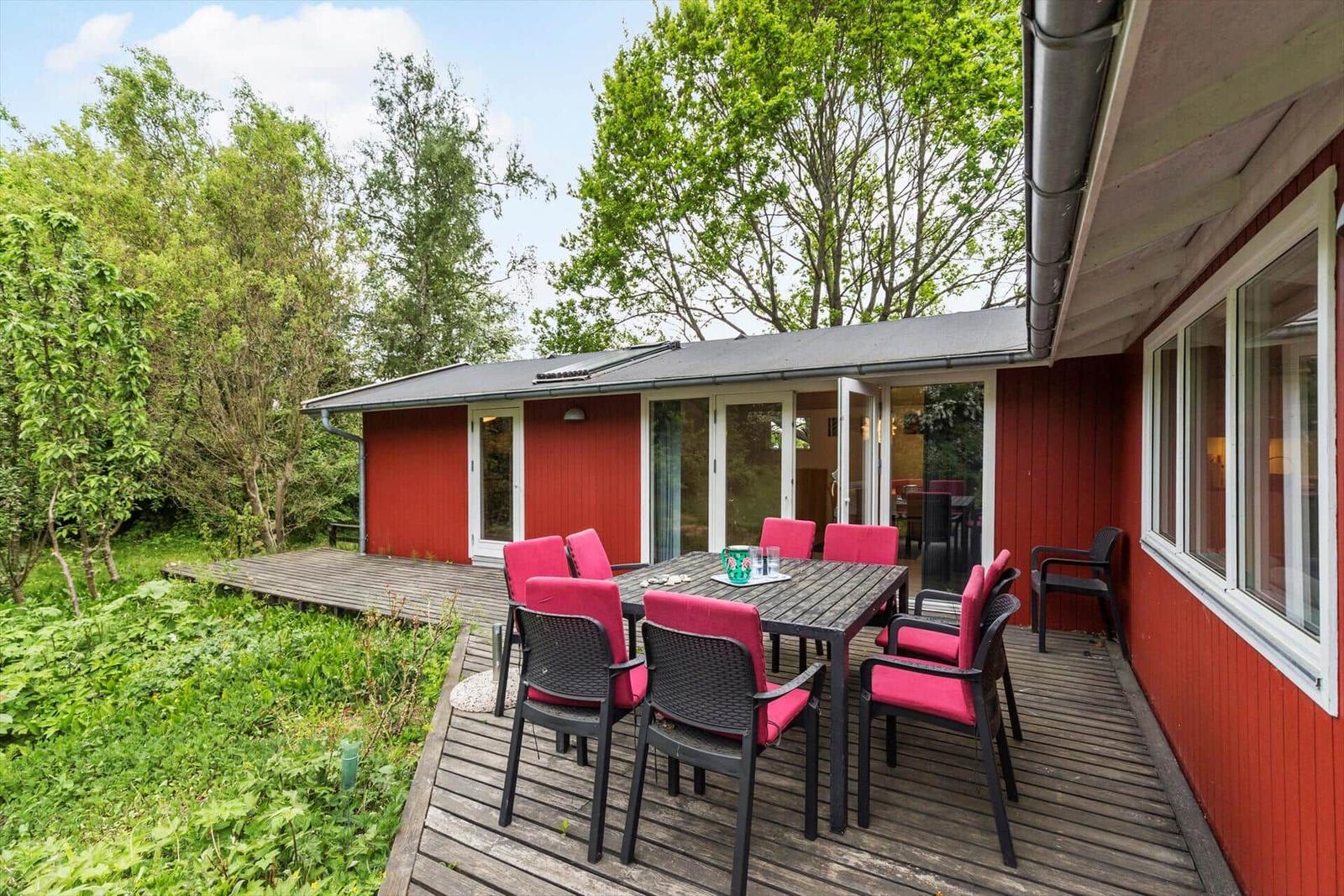 Roter Holzhaus mit Terrasse, Tisch und Stühlen im Garten.