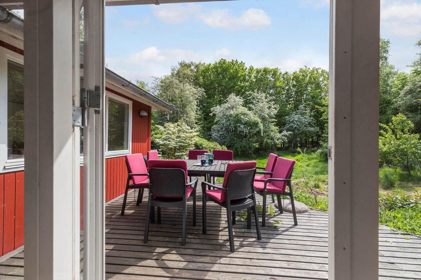 Terrasse mit Tisch und Stühlen, Blick auf grüne Bäume und einen roten Holzhausabschnitt.