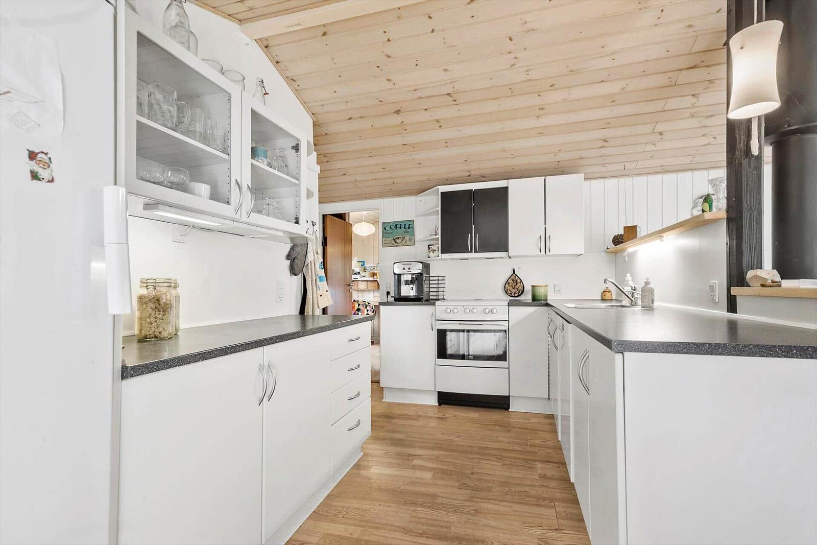 Küche mit weißen Schränken, dunklem Arbeitsplatz und Holzdecke.