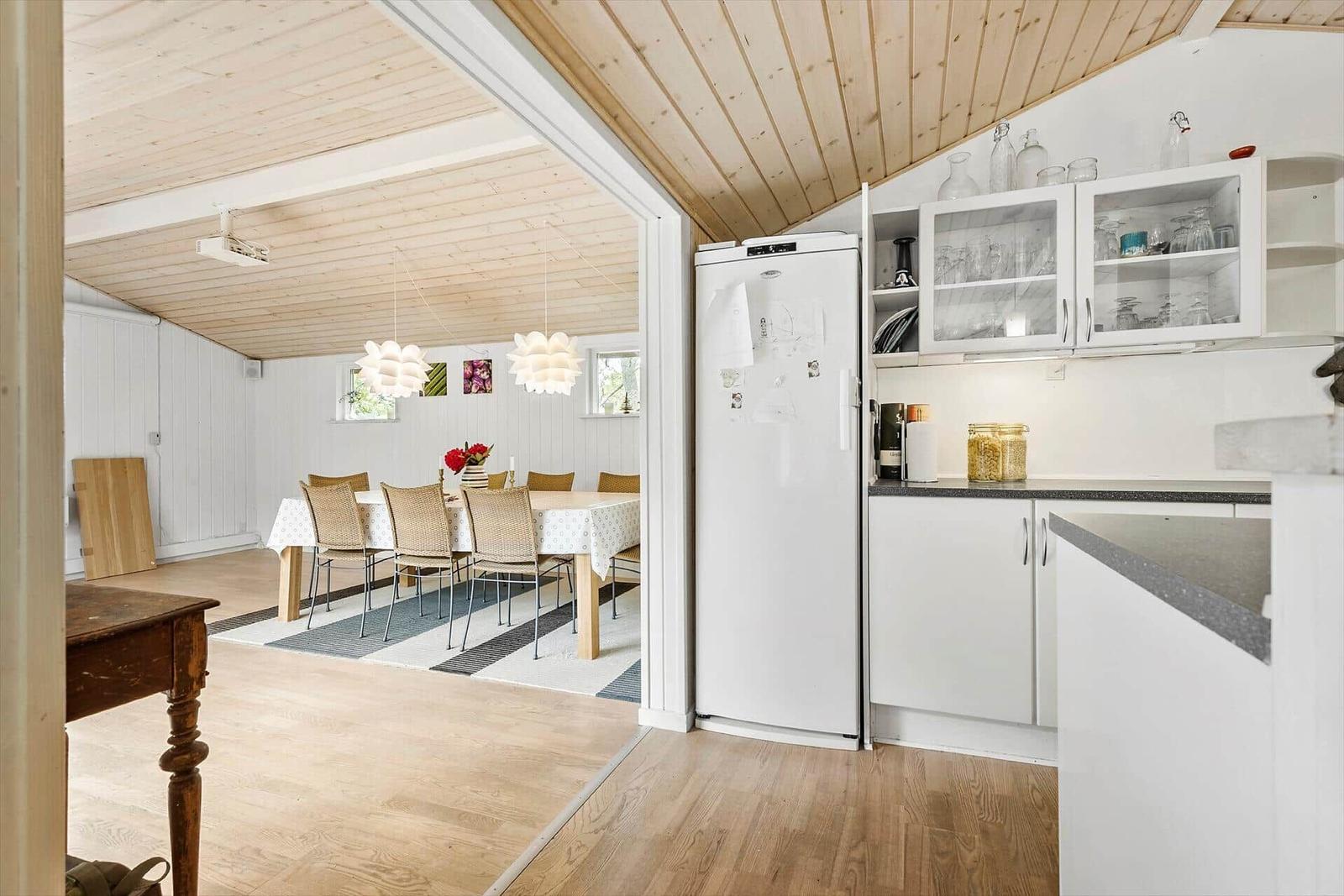 Küche mit Kühlschrank und Glasregalen. Durchgang zur Essnische mit Tisch und Stühlen.
