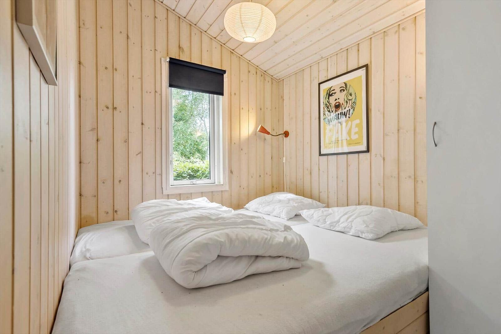 Schlafzimmer mit Holzwand, Bett und Fenster mit Blick auf Grün.