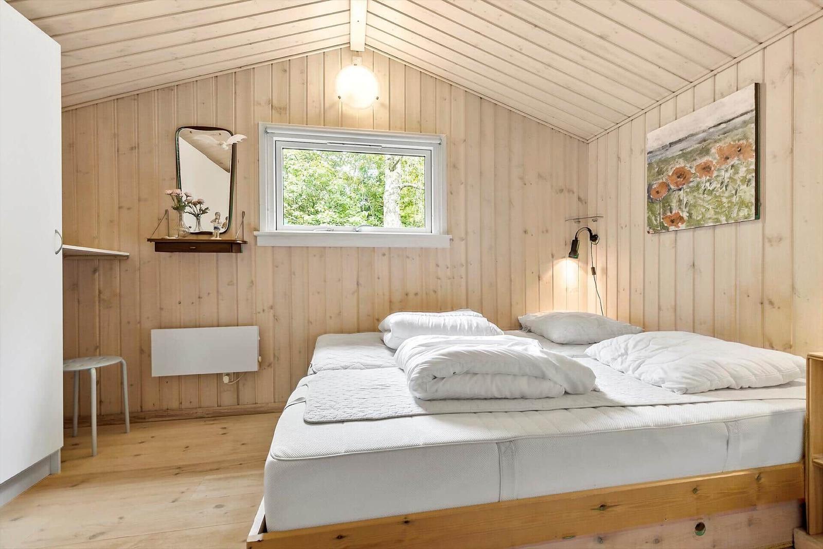 Schlafzimmer mit Holzwand, Bett und Fenster zur Natur.