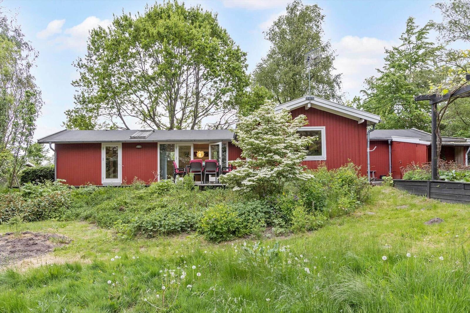 Rotes Haus mit Terrasse und Garten unter Bäumen.