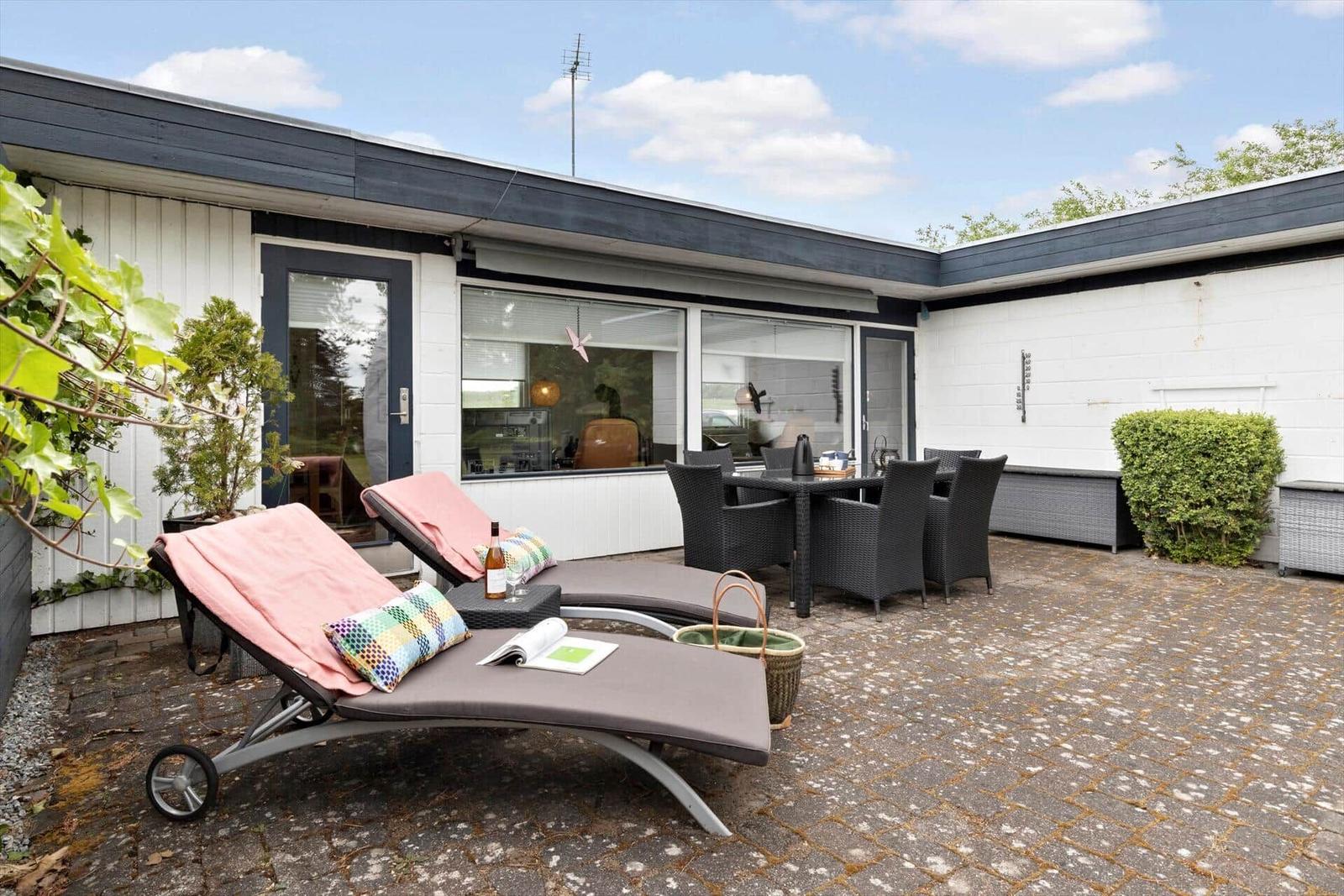 Terrace with loungers, table, and chairs. House with windows and plants.