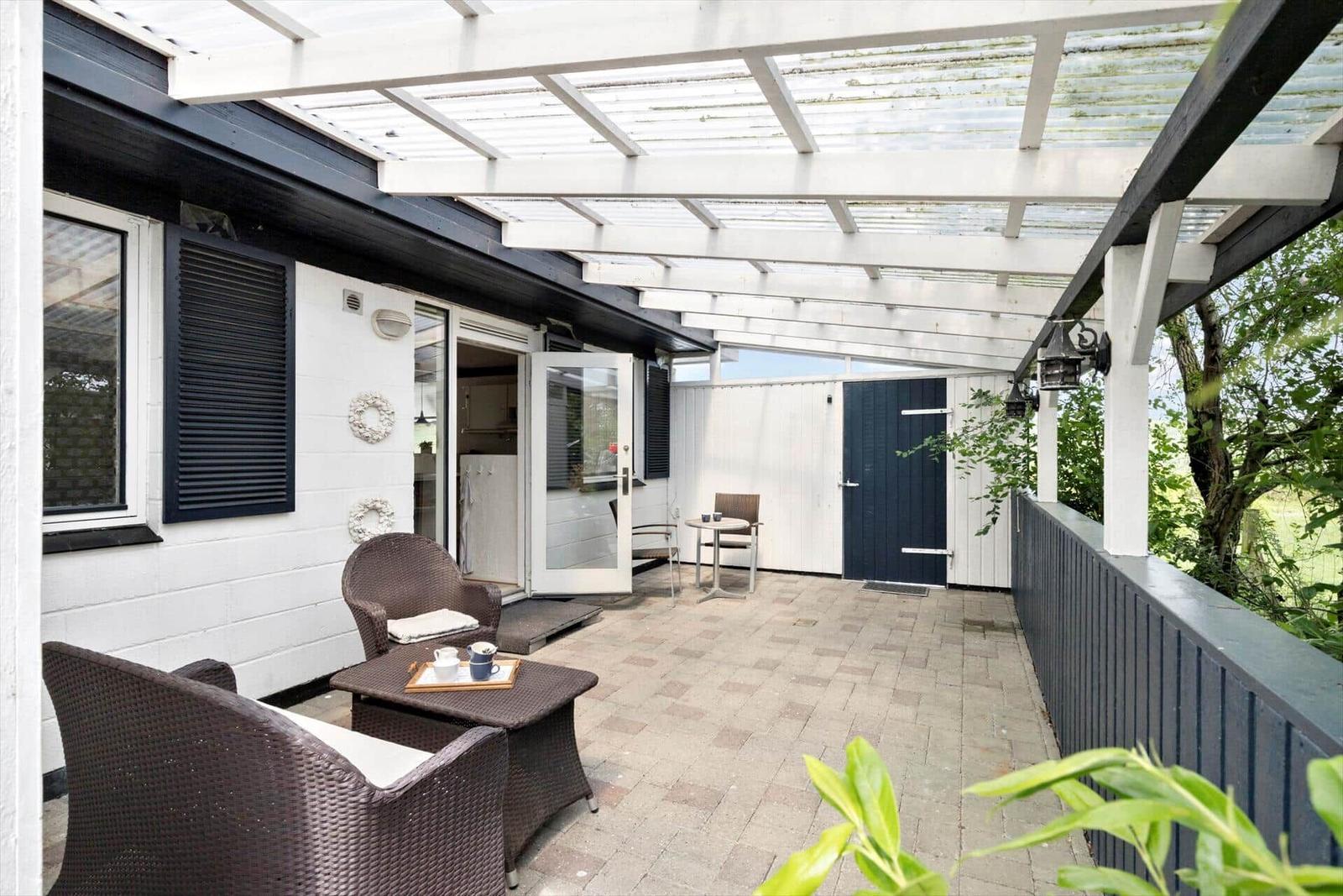 Terrace with seating under roof, view of garden and house.