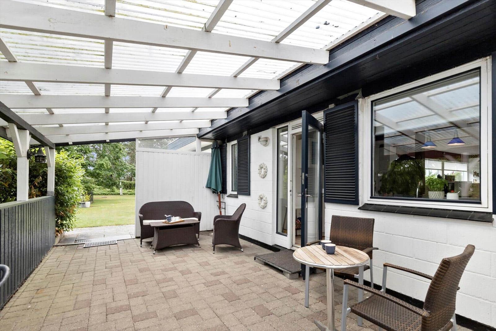 Terrace with seating under roof, paved floor, and view of garden.
