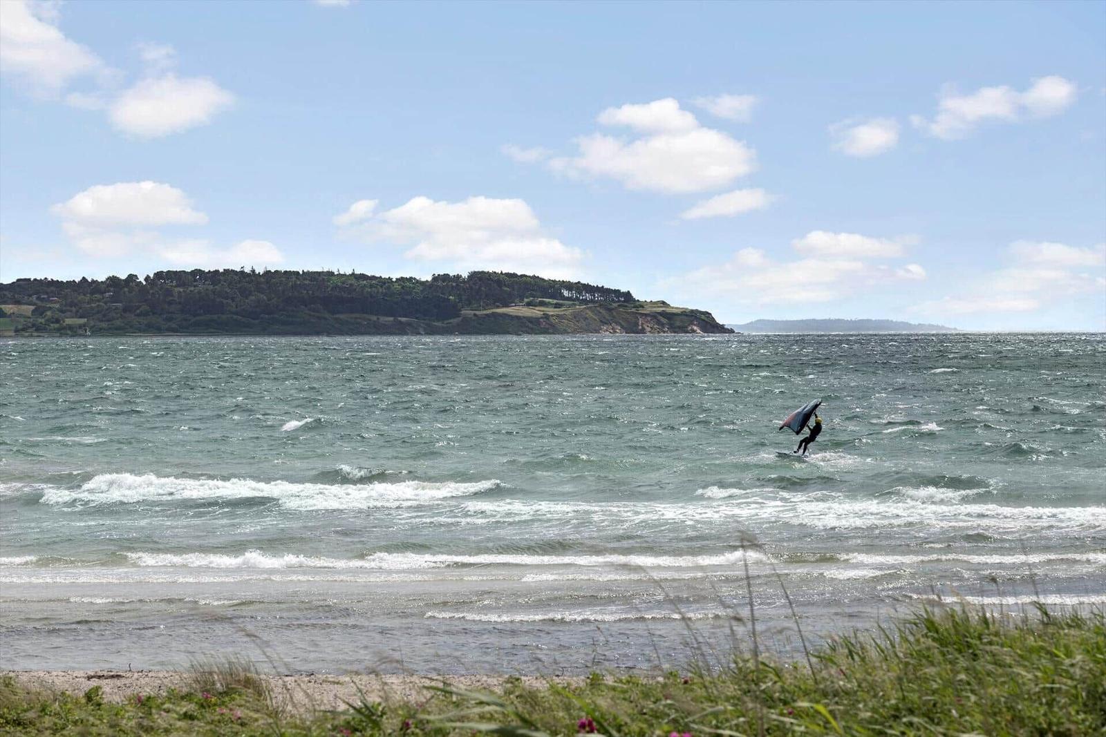 Kitesurfer on water near a wooded coastline under blue sky.