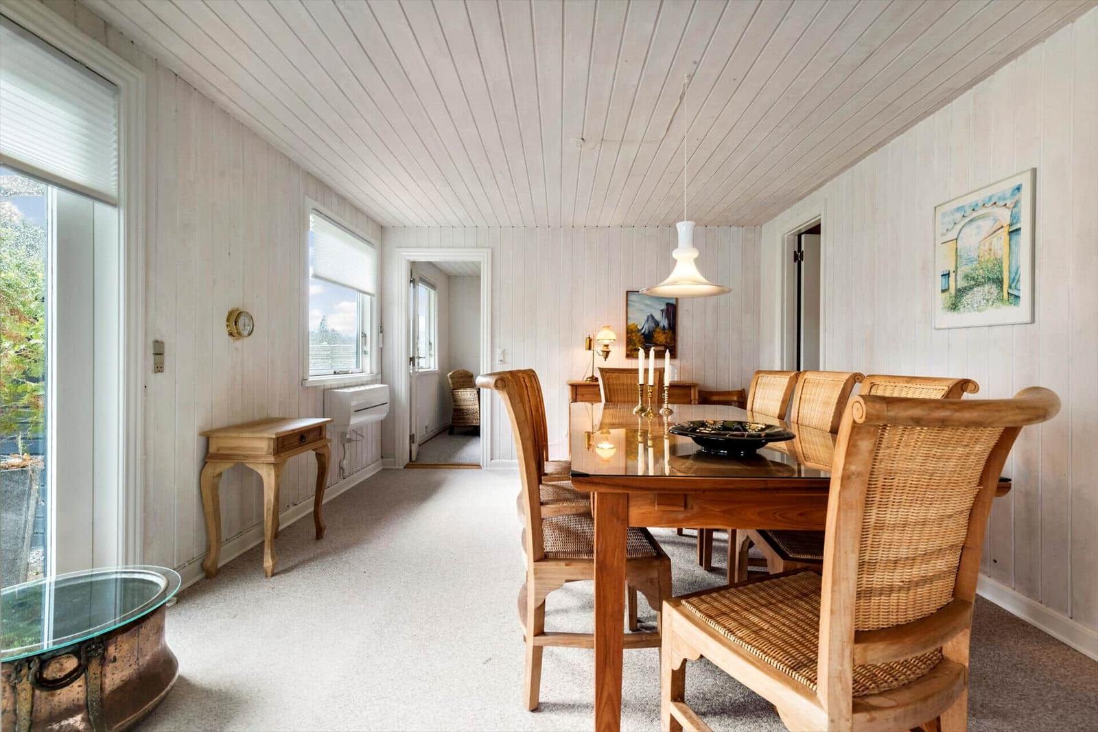 Dining room with wooden table, chairs, and large windows. White wood walls and ceiling.