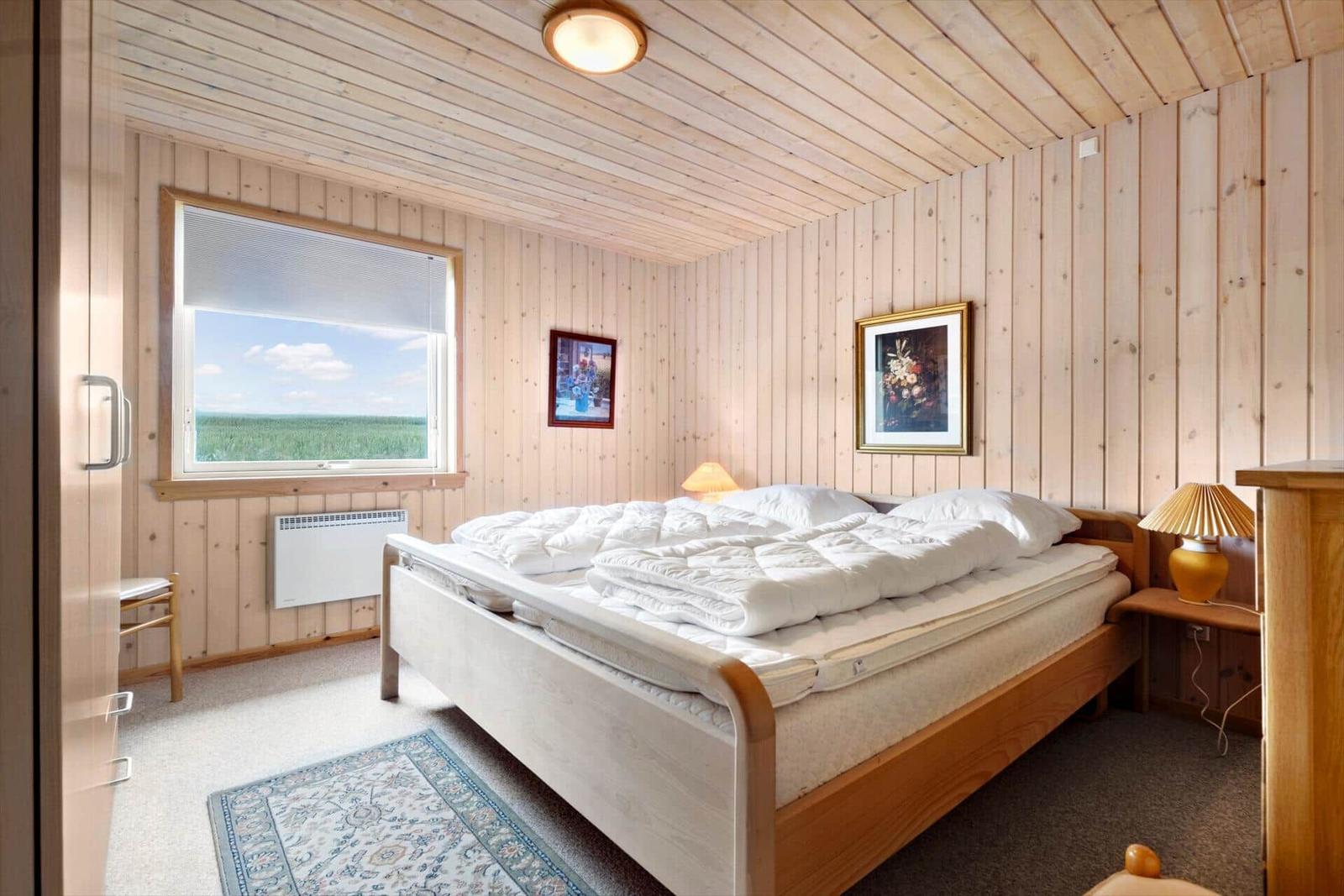 Bedroom with wooden walls, bed, window, and rug