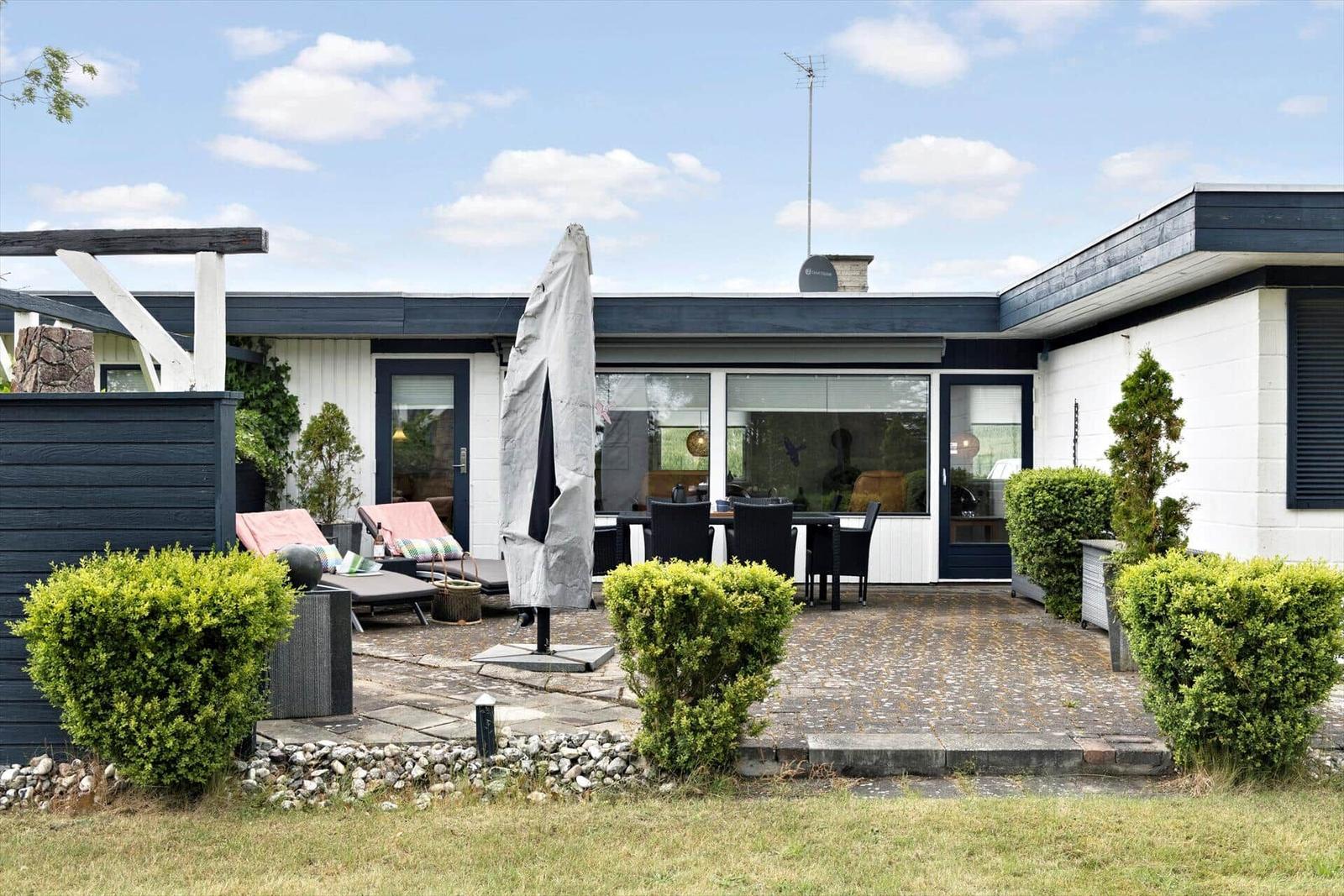 Terrace with lounge furniture and dining table under a closed umbrella.