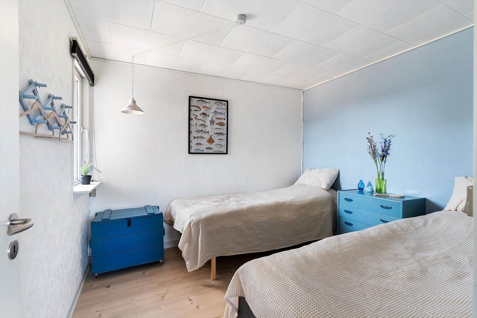 Zwei Betten, blaue Schubladenkommode, Wandbild mit Fischen, Fenster mit Pflanze.
