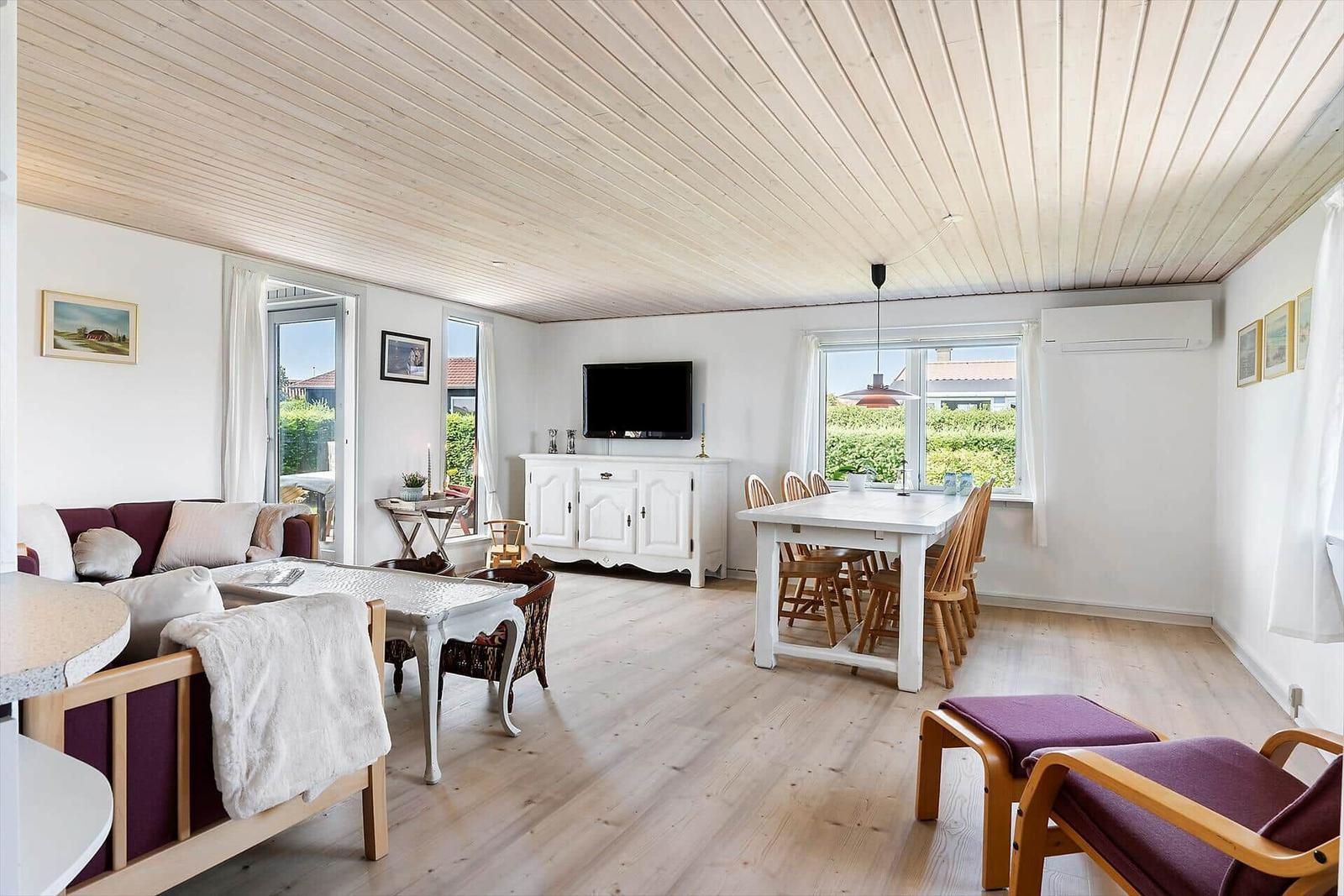 Wohn- und Essbereich mit Holzboden, TV, Tisch und Stühlen, Fenster mit Blick auf Garten.