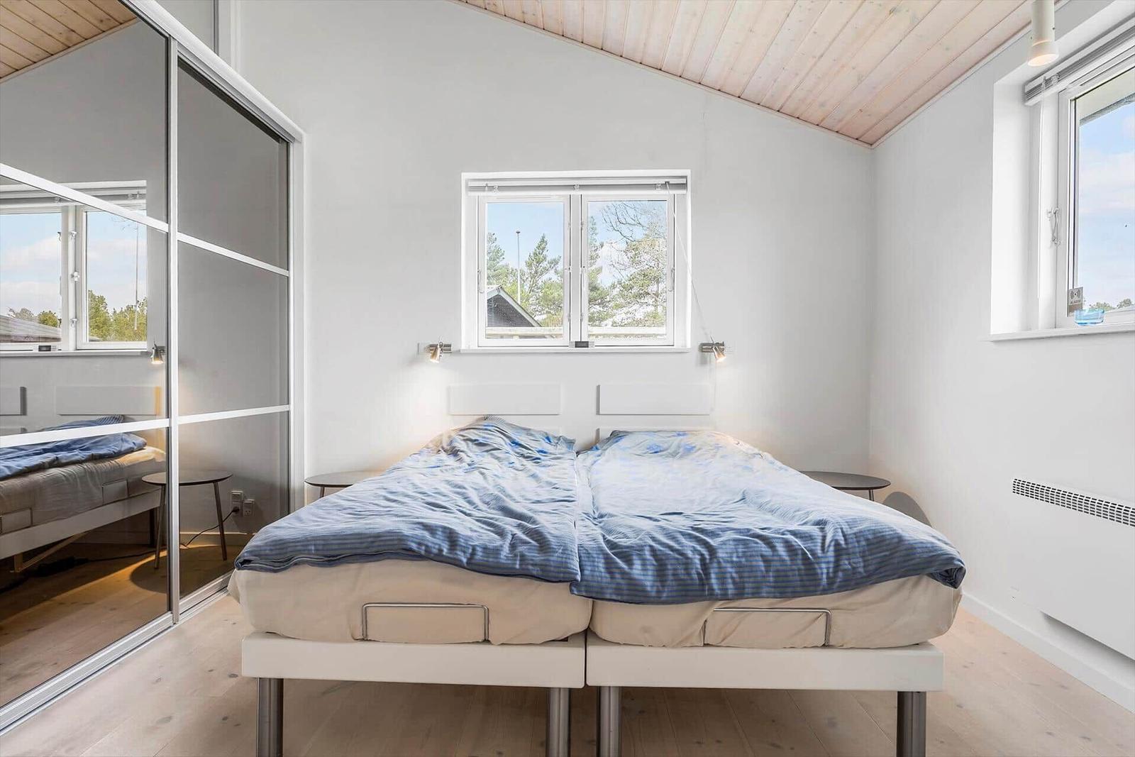 Schlafzimmer mit Doppelbett, Fenstern und Spiegelschrank.