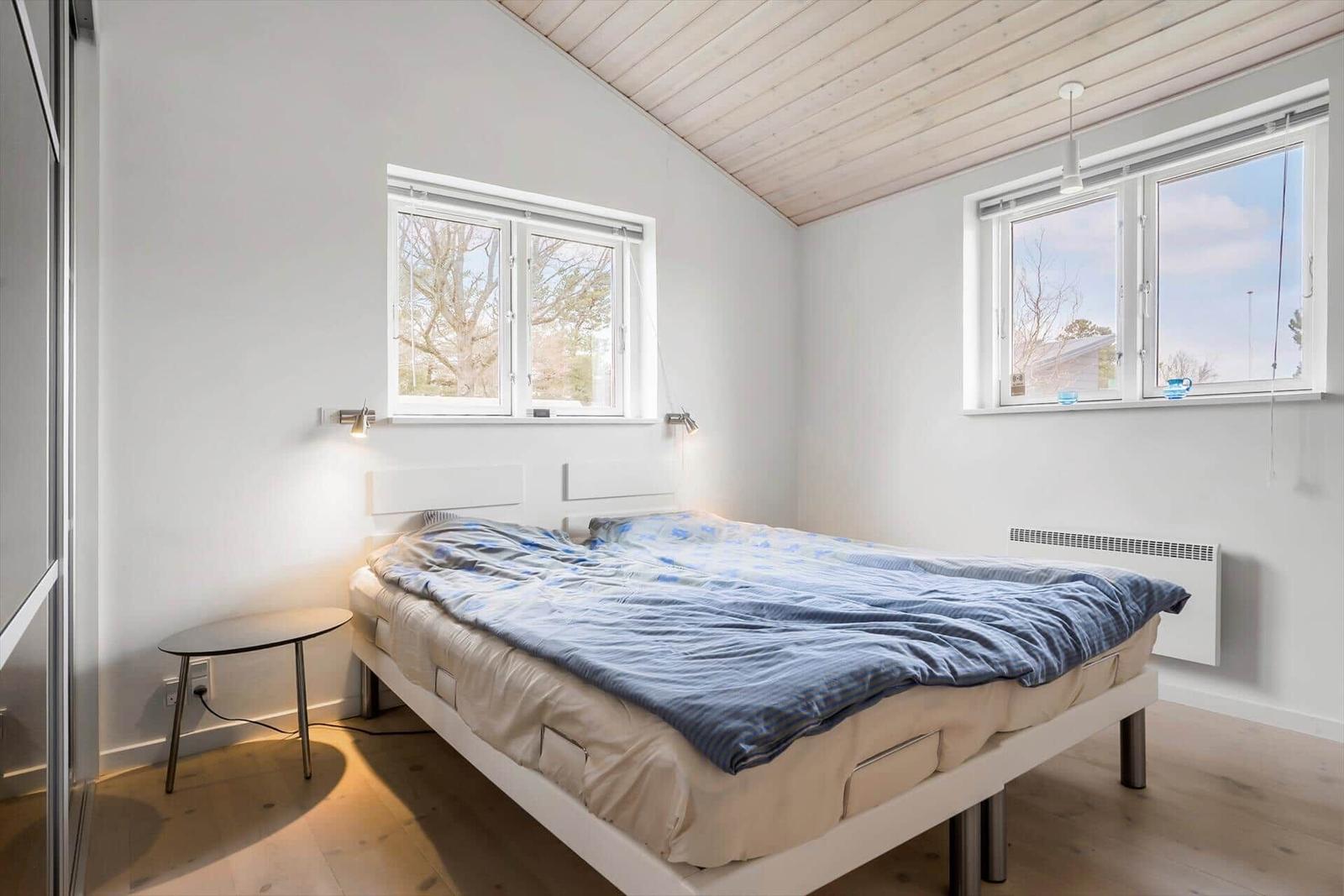 Schlafzimmer mit Bett, zwei Fenstern und Holzboden.