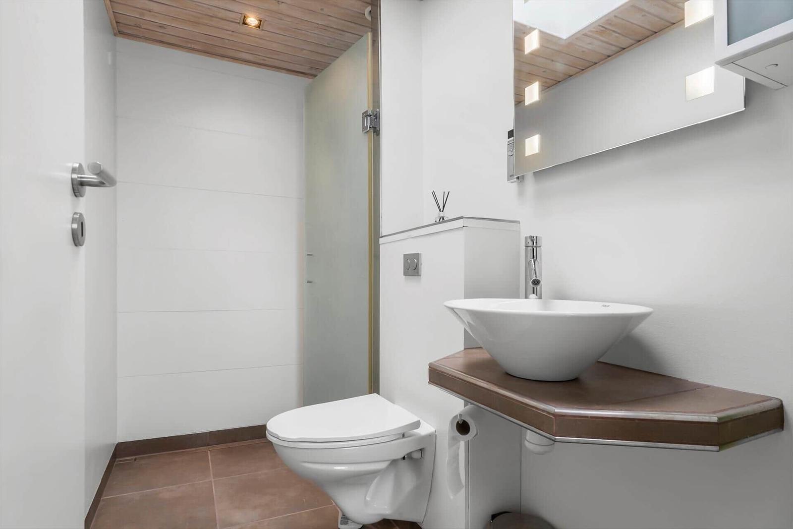 Bad mit Dusche, Toilette und Waschbecken auf Holzunterlage.