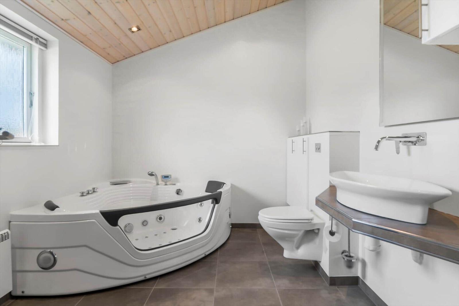 Bad mit Whirlpool, Waschbecken und Toilette unter Holzdecke.