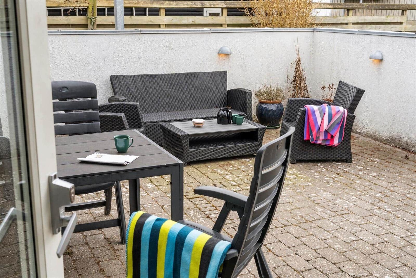 Terrasse mit Gartenmöbeln, Tisch und Stühlen. Beleuchtung an der Wand. Pflanzen und Decken.