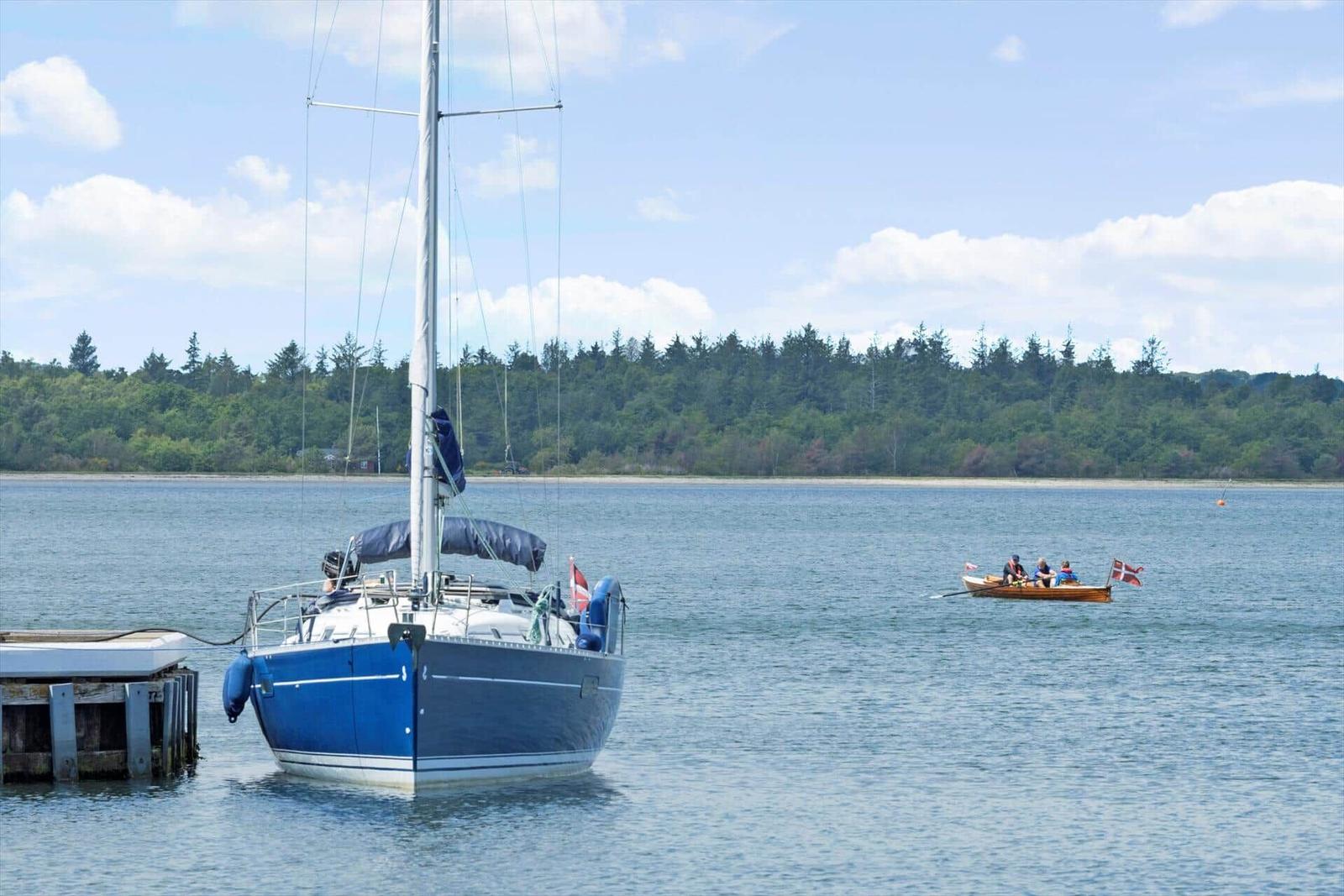 Ein Segelboot liegt am Steg. Ein Ruderboot mit Flagge fährt auf dem Wasser.