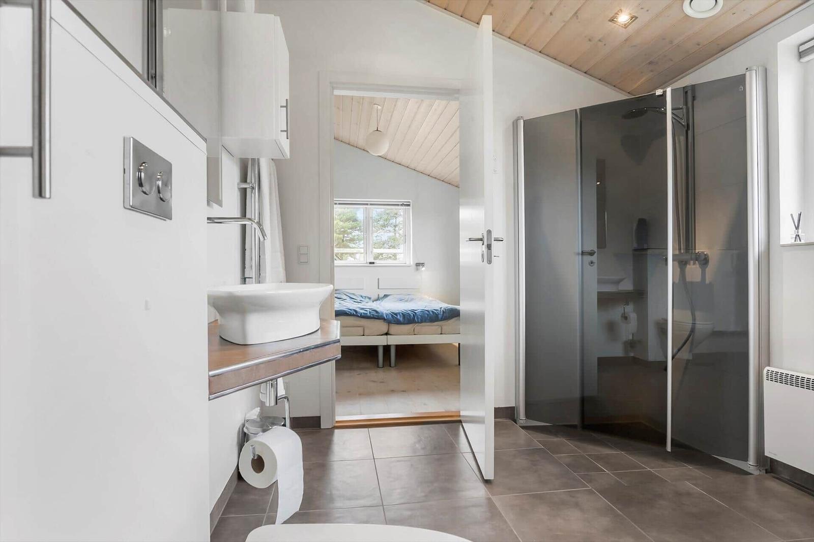 Badezimmer mit Dusche und Blick in Schlafzimmer mit Bett und Fenster.