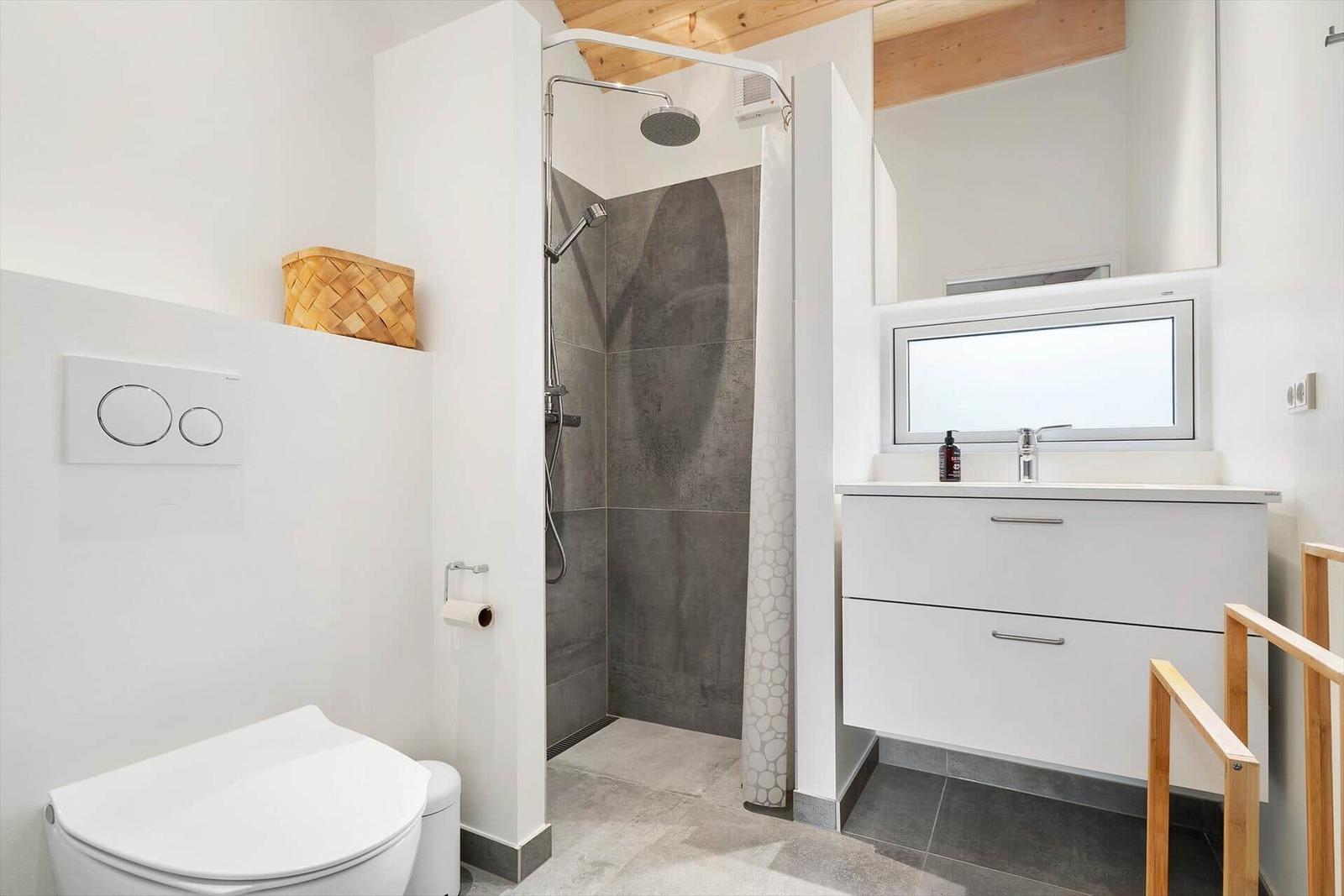 Badezimmer mit Dusche, Waschbecken und Toilette. Holzdecke und weiße Flächen.