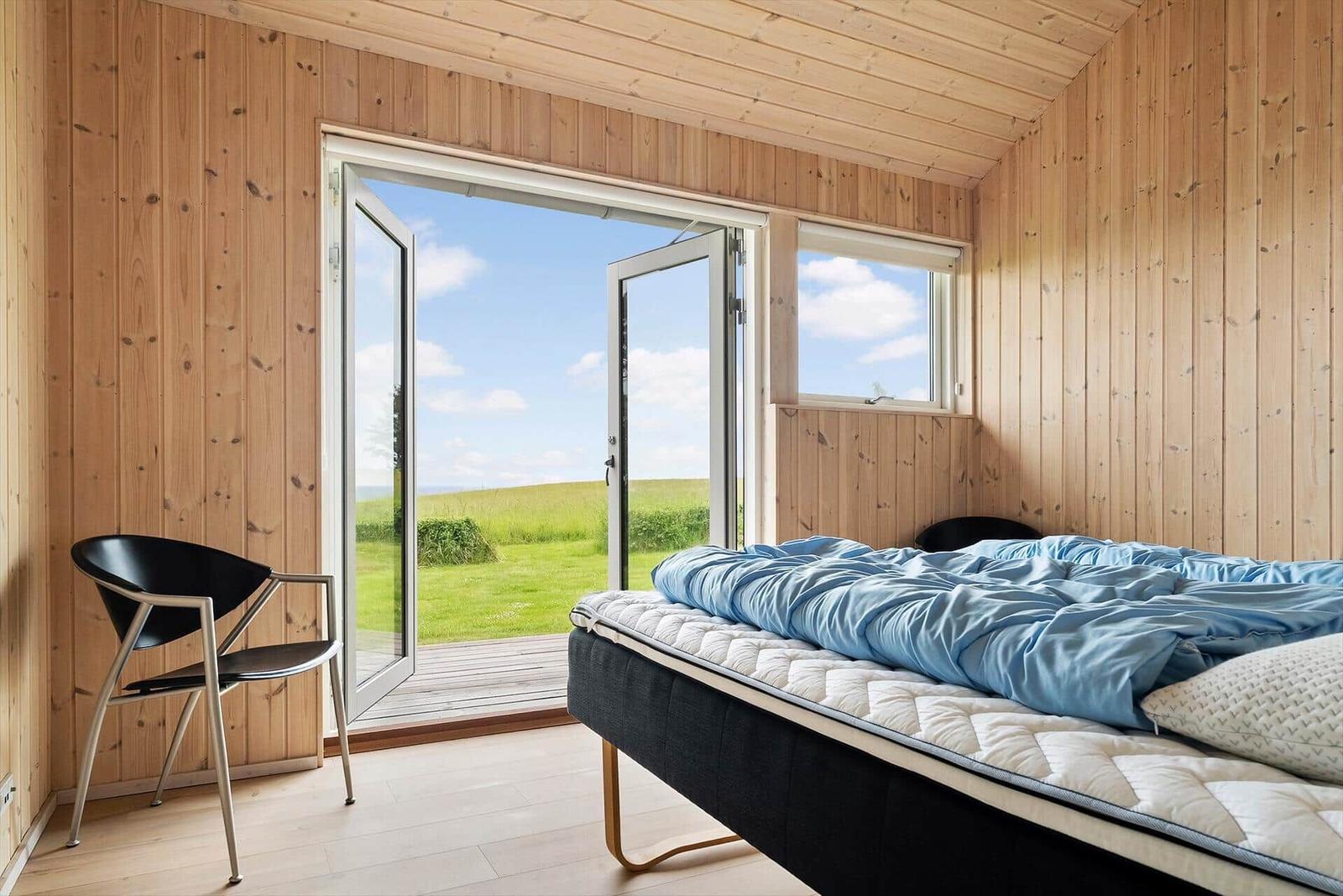 Schlafzimmer mit Bett, Stuhl und Blick auf Grünfläche.