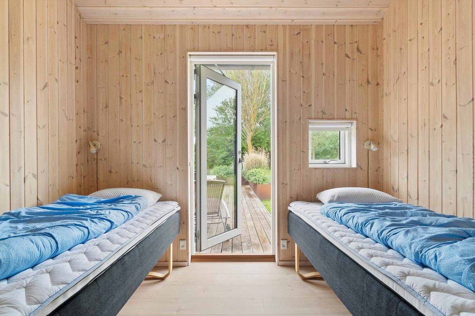 Zwei Betten mit blauen Decken, Holzwände und Tür zum Garten.